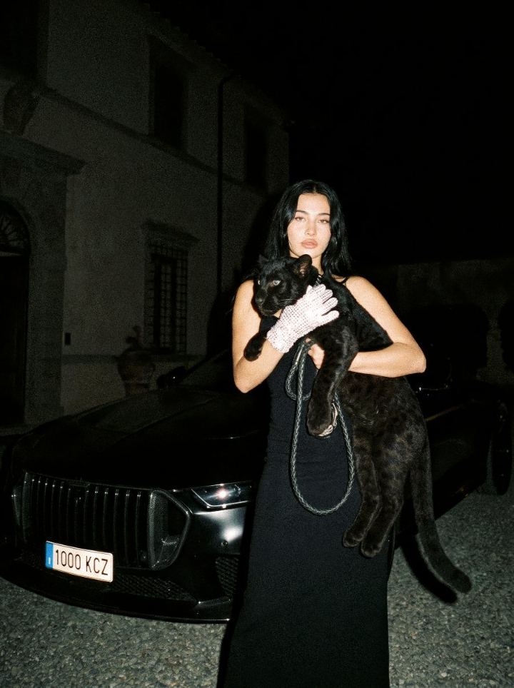 Woman in a black gown holding a black panther in front of a black Mercedes