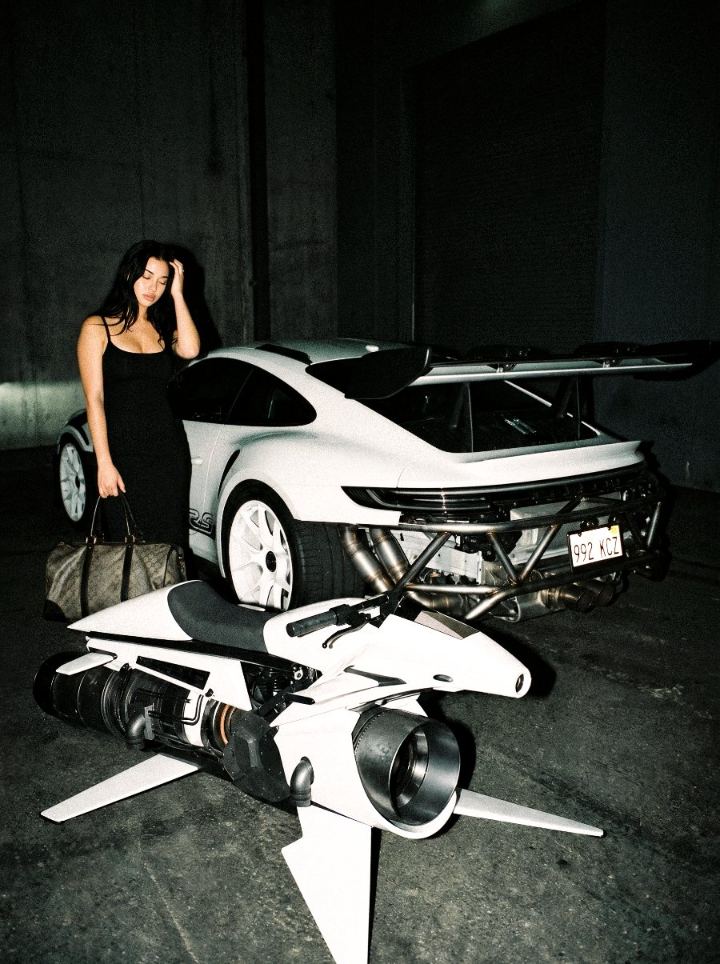 Woman in a black dress beside a white Porsche GT3 RS and a jet-engine motorbike